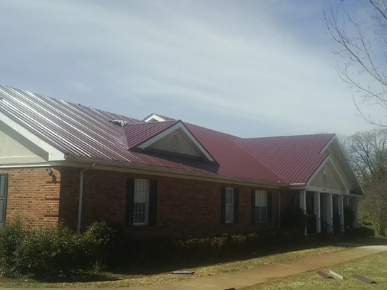 Red metal roof with gabled entries on a long brick building, from a Hail Damage Roof Repair job in Terrell