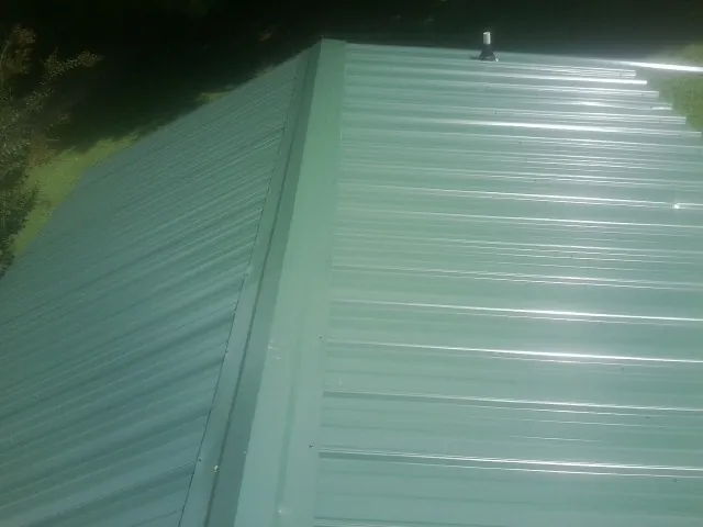 New green metal panels meeting at the ridge of a roof — Flat Roof Repair work by our crew in Terrell