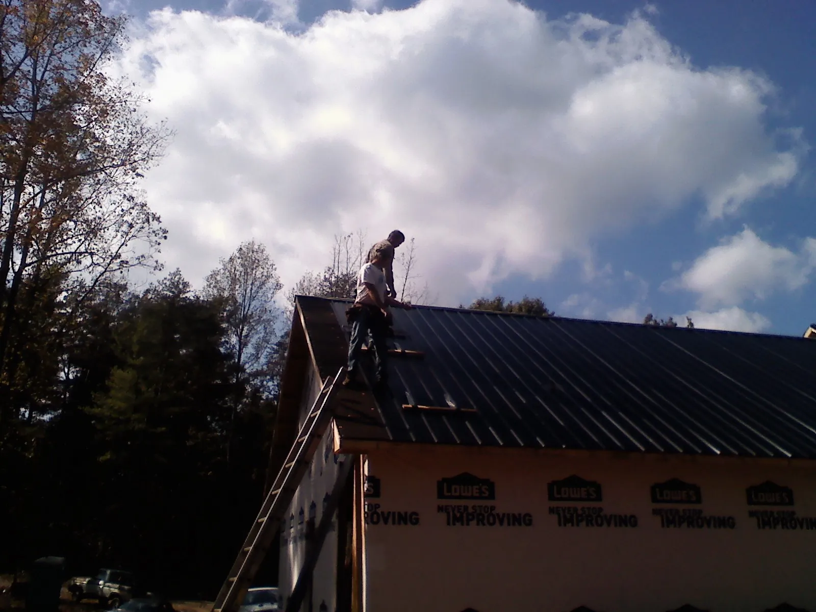 Roofer fastening dark metal panels high against a cloudy sky, from a Roof Inspection job in Terrell